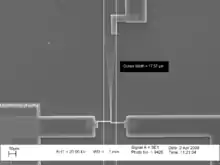 A photomicrograph of a vibrating cantilever. Cursors on the picture indicate that the peak-to-peak amplitude of the vibration is 17.57μm.